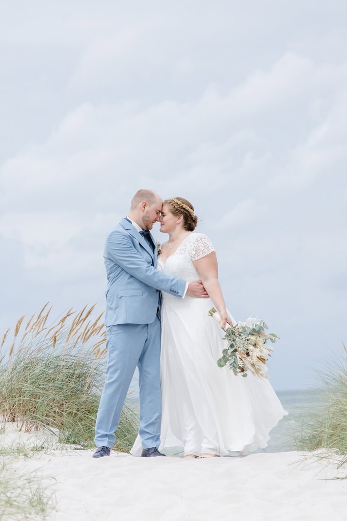 Brautpaar steht umarmt am Stand zwischen den Dünen an der Ostsee, fotografiert von Photography Team