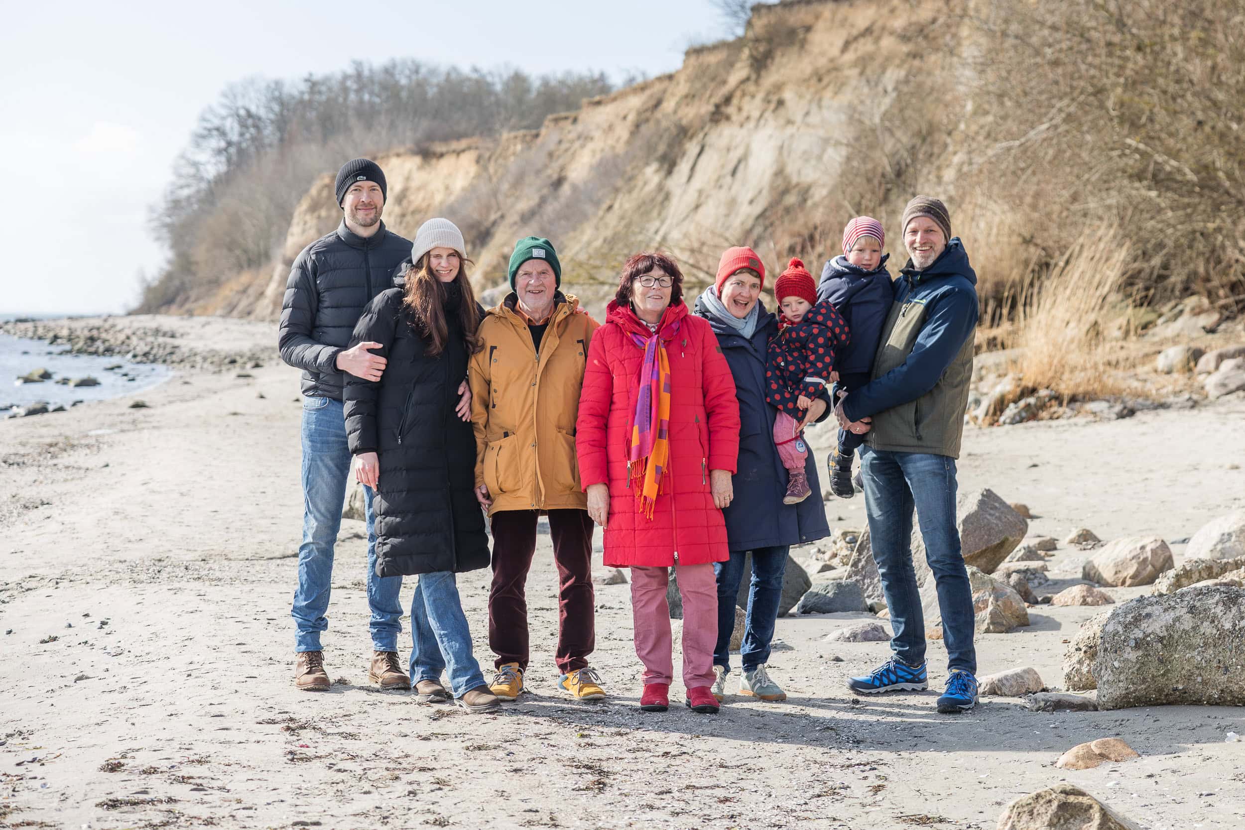 Großfamilie mit zwei Kindern und Großeltern steht gemeinsam am Strand von Grömitz, im Hintergrund die Steilküste