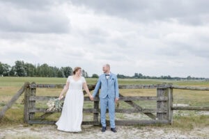 Brautpaar steht Hand in Hand am Weidegatter in Stein an der Ostsee, lacht sich glücklich an, Salzwiesen im Hintergrund